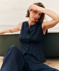Woman wearing a navy blue sleeveless top with blue pants sitting on a ledge.