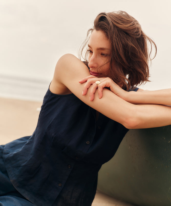 Woman sitting on a beach wearing a blue top and pants.