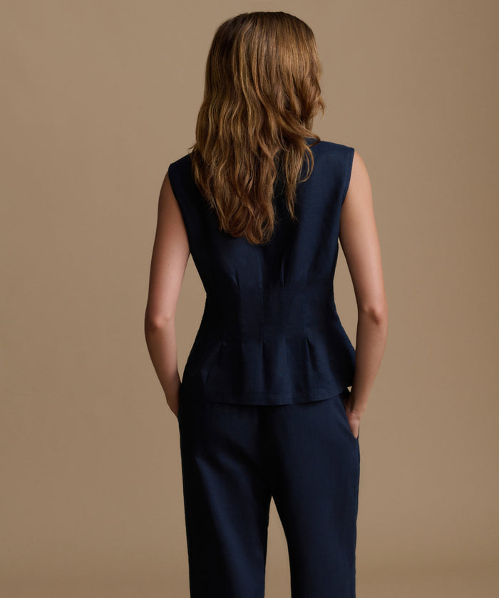 Woman wearing a navy sleeveless top and pants against a beige background