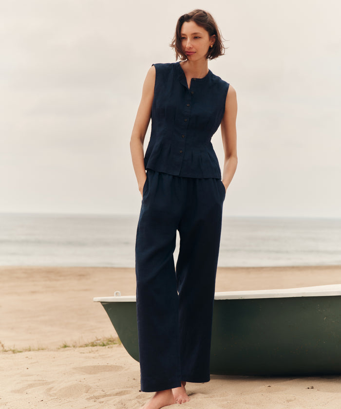 Woman wearing a navy sleeveless top and navy pants standing at the beach.