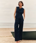 Woman wearing a navy sleeveless top and navy pants standing at the beach.