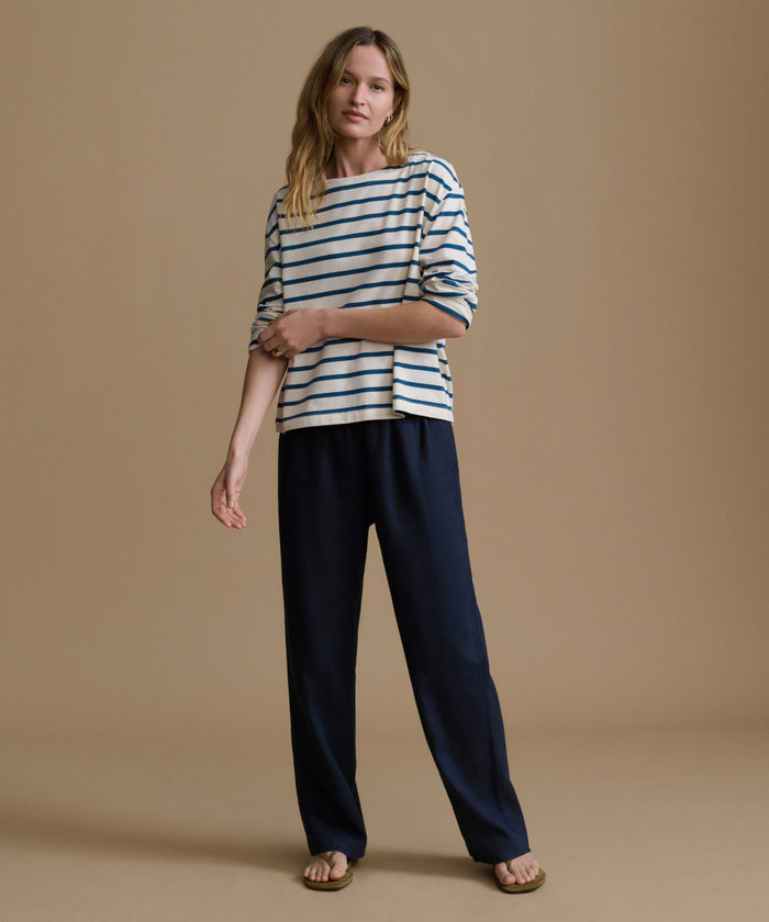 Woman wearing a striped shirt and navy pants on a brown background