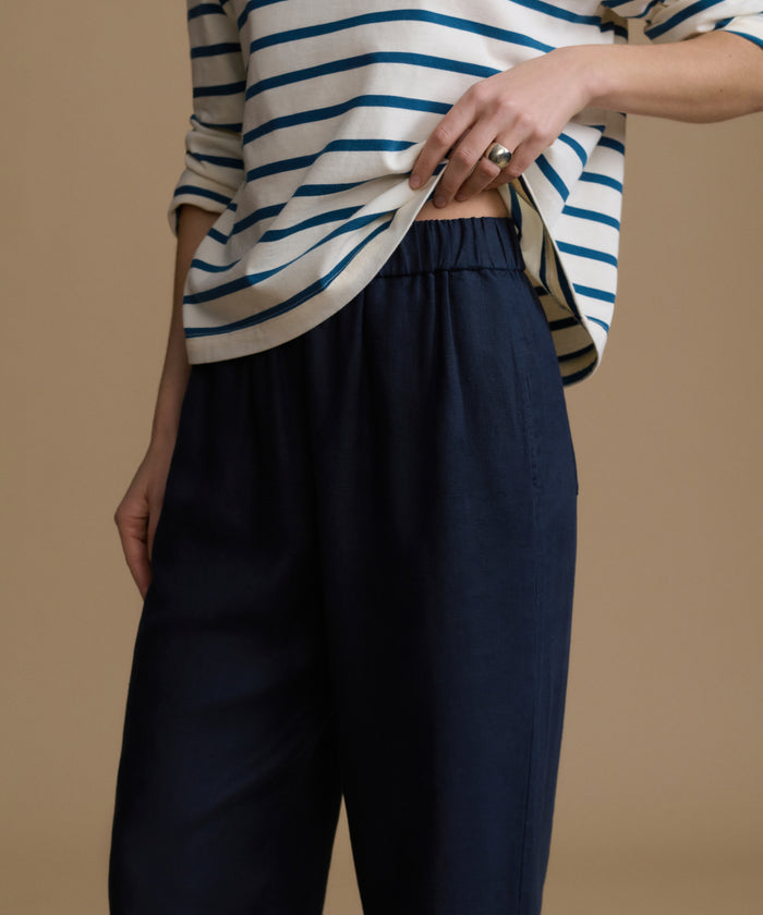 Woman wearing a striped shirt and navy pants on a brown background