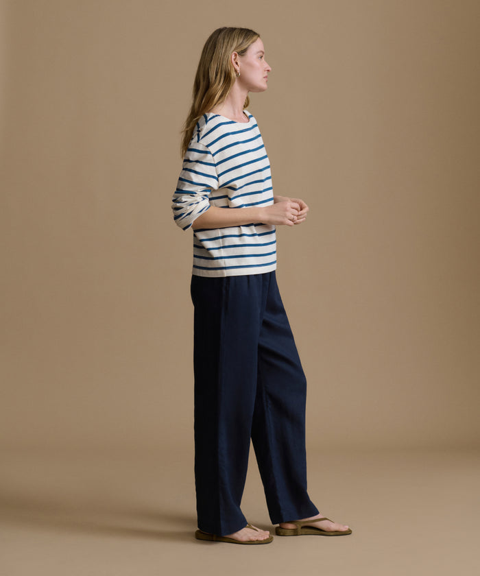 Woman wearing a striped shirt and navy pants on a brown background