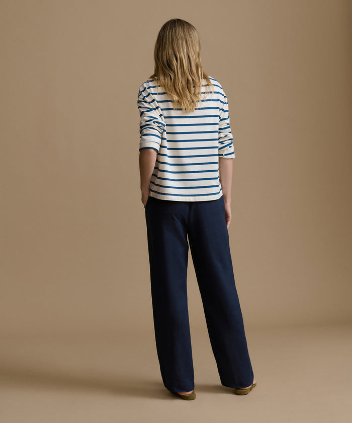 Woman wearing a striped shirt and navy pants on a brown background
