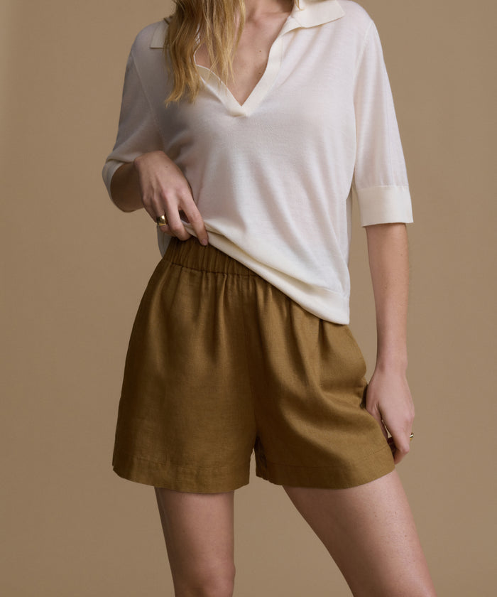 Person wearing a white shirt and brown shorts on a beige background