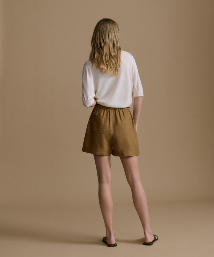 Woman wearing a white shirt and brown shorts against a beige background