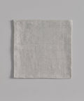 A neatly folded light gray Linen Tablecloth featuring thin horizontal stripes and a subtle black stripe, displayed on a flat light gray background.