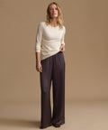 A woman modeling a cream long-sleeve knit top and dark charcoal wide-leg satin pants against a solid beige studio background.