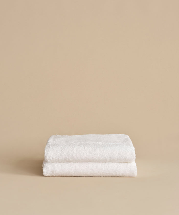 Two neatly folded Loom Bath Sheets, crafted from a luxurious cotton modal blend, are stacked on top of each other against a plain beige background.