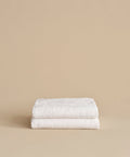 Two neatly folded Loom Bath Sheets, crafted from a luxurious cotton modal blend, are stacked on top of each other against a plain beige background.
