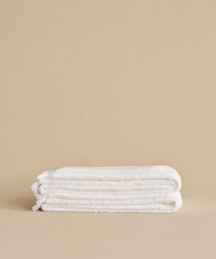 The Loom Bath Sheet, ultra-soft and white, is neatly folded on a neutral beige surface with a plain beige background.