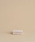The Loom Hand Towel, made from soft cotton modal in beige, is neatly folded and placed on a matching surface and background, creating a calm and minimalistic look.