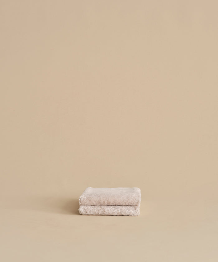 The Loom Hand Towel, made from soft cotton modal in beige, is neatly folded and placed on a matching surface and background, creating a calm and minimalistic look.