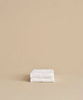 Two super-soft Loom Hand Towels, neatly folded and stacked against a plain beige background, make a perfect bathroom essential.