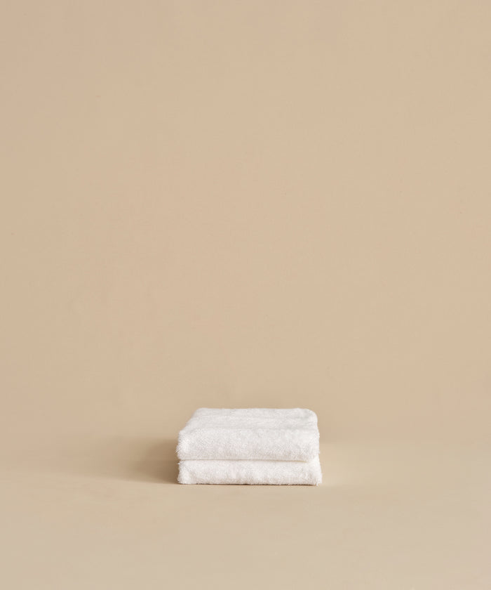 Two super-soft Loom Hand Towels, neatly folded and stacked against a plain beige background, make a perfect bathroom essential.