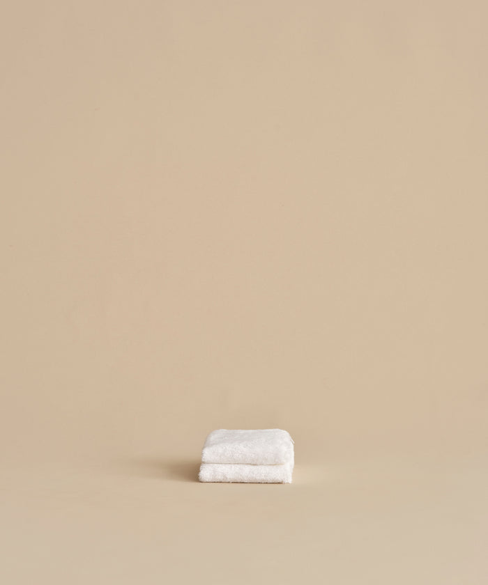 The Loom Wash Cloth, neatly folded, rests on a plain beige surface with a matching background, showcasing a minimalist and clean bathroom essential.