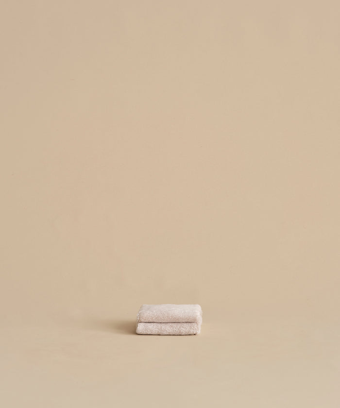 The Loom Wash Cloth, a small and super-soft beige essential, is neatly folded on a matching surface with a plain beige background—perfect for any bathroom.