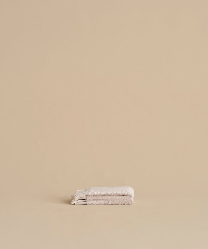 A neatly folded Loom Wash Cloth in super-soft light beige rests on a matching surface with a plain beige background, creating a minimalist and serene look—ideal as a bathroom essential.