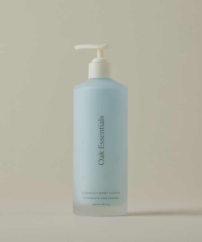 A blue bottle of Luminous Body Lotion with a white pump dispenser sits on a beige surface, featuring a modern label that hints at nourishing ingredients for radiant skin.