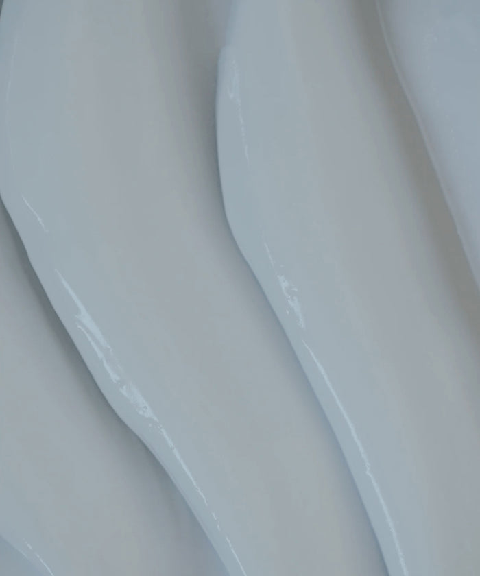 Close-up of Luminous Body Lotion’s smooth, glossy white surface with gentle, wavy ridges running diagonally for a soft, flowing texture.