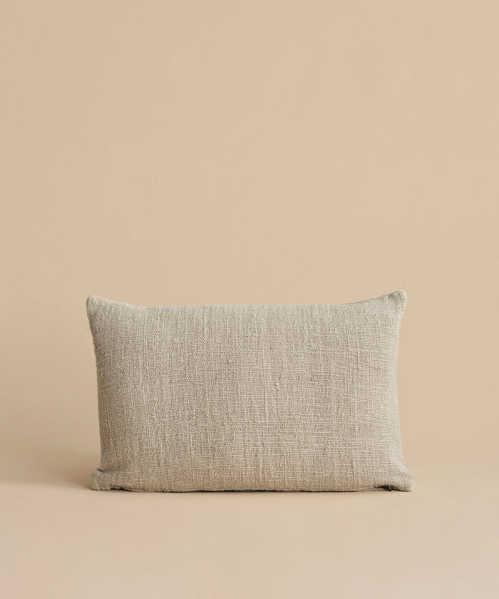 The Luna Lumbar Pillow, featuring a textured beige fabric cover and feather down insert, is placed against a matching beige background.