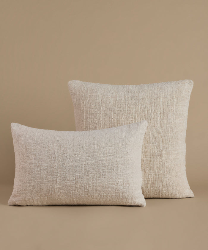 A textured cream color pillow against a beige background.