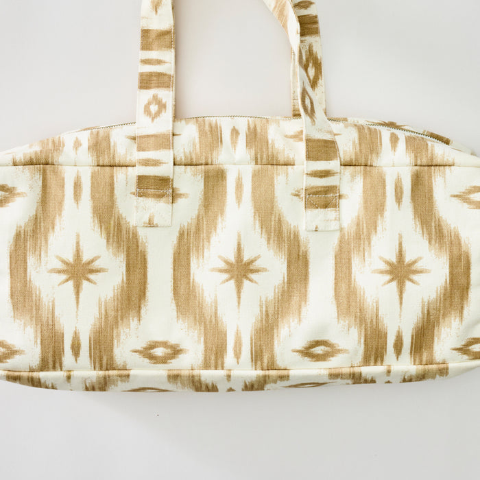 A rectangular fabric bag featuring a sand and white ikat pattern with starburst motifs and two matching carrying handles.