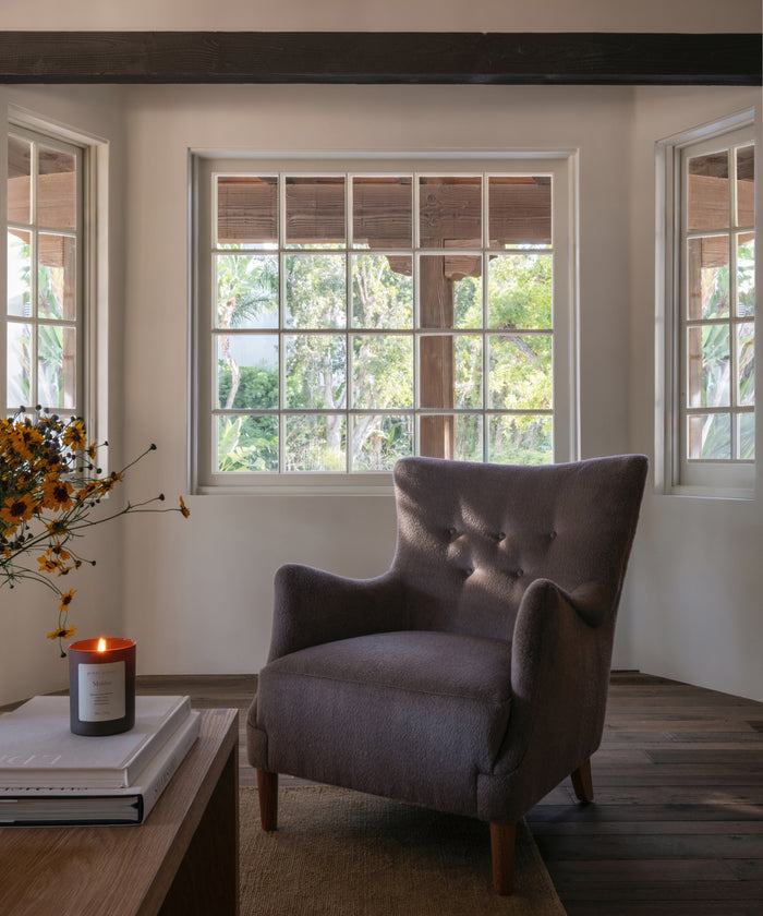 A candle on a wood coffee table with an accent chair in a living room setting.