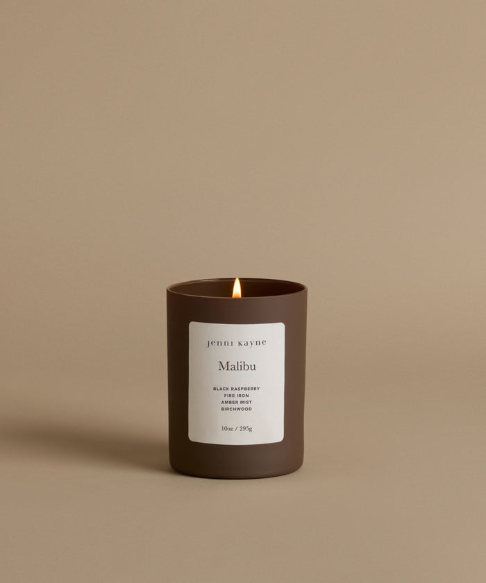 A lit candle in the scent Malibu against a beige background.