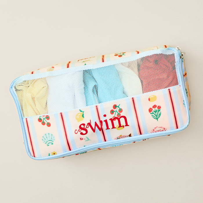 Top-down view of a rectangular, zippered Medium Packing Cube in the "Dolce Vita" print. The cube features a clear mesh top section and a patterned lower section decorated with small illustrations of lemons, tomatoes, flowers, and seashells on a striped background.