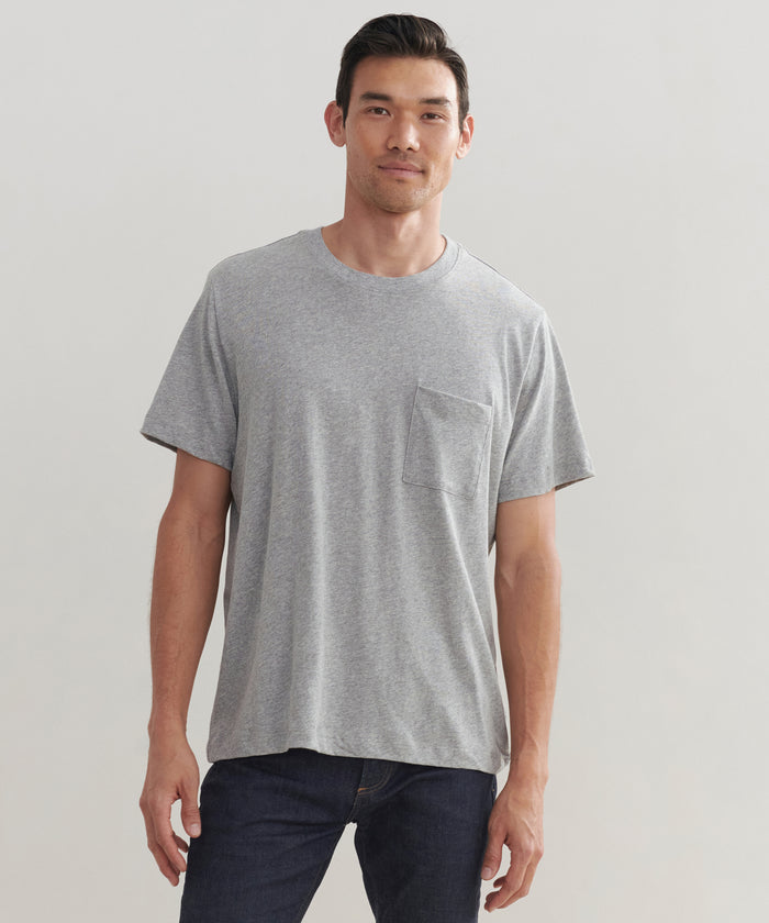 A man faces forward, wearing the Mens Vintage Pocket Tee in grey with a chest pocket and dark blue jeans, set against a plain light background.