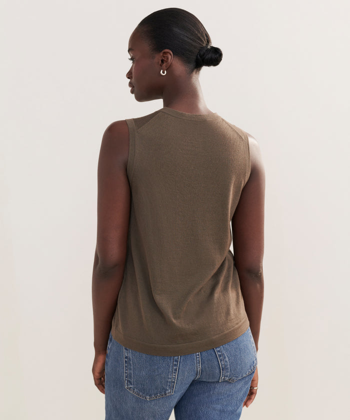 A woman with dark skin and hair in a low bun models the Merino Tank, paired with blue jeans, as she stands with her back to the camera against a plain light background.