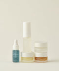 The Mini Routine by Five Oak Essentials features a dropper bottle, pump bottle, and three jars in various sizes with white and amber accents—perfect travel skincare companions arranged on a neutral background.