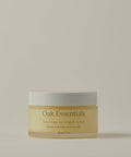 A frosted glass jar with a white lid labeled Moisture Rich Body Balm rests on a light beige background. The label, in English and French, highlights nourishing ingredients such as Cocoa Butter.