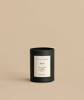 A Musk Glass Candle with a white label reading jenni kayne, Musk, Spicy Cardamom, Sandalwood, Orchid, 10oz / 283g sits on a beige surface. This hand-poured coconut soy wax candle is made in Los Angeles and matches the background.