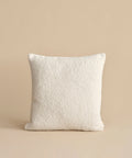 The Nell Boucle Pillow—a square, textured ivory accent—is centered against a plain beige background.