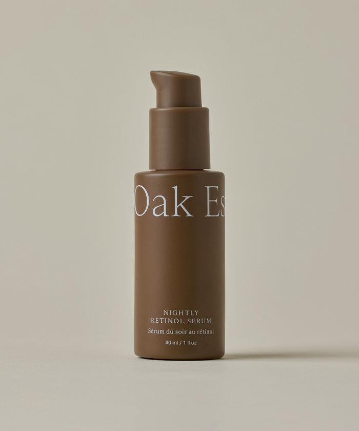 A brown bottle with a pump dispenser labeled "Nightly Retinol Serum," designed for hydration and reducing fine lines, is displayed against a plain light beige background.