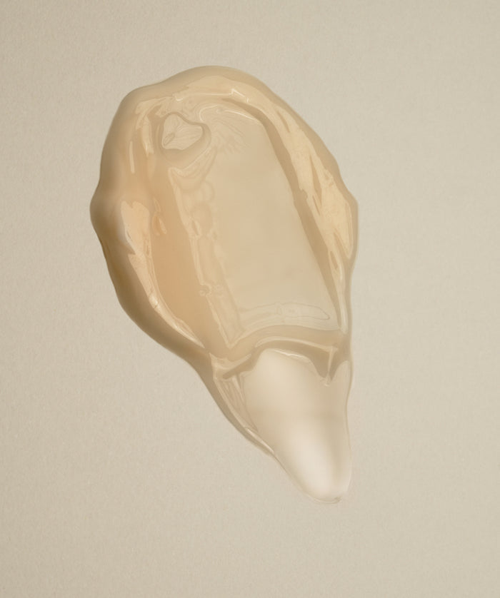 A translucent, beige liquid blob on a neutral background resembles an oyster shell—capturing the smoothing power of Nightly Retinol Serum for fine lines.