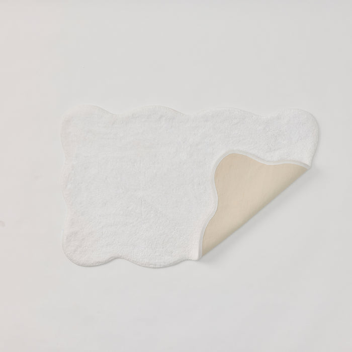 White scalloped bath rug with a corner folded over to reveal the beige non-slip backing.