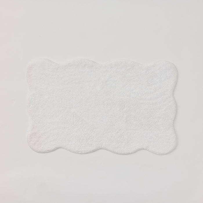 A plush white bath rug with scalloped edges.