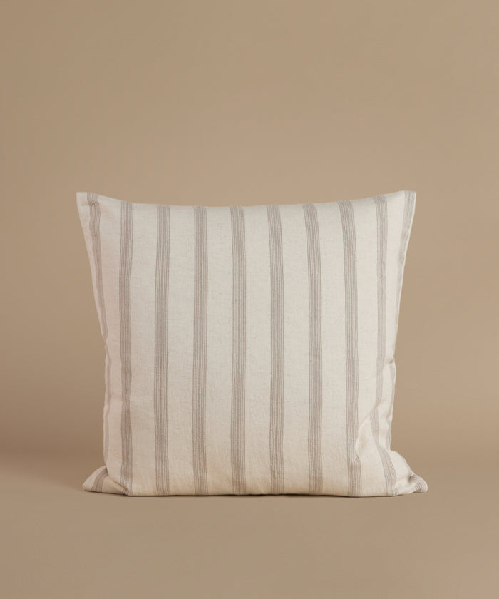 A white and tan stripe pillow against a beige background.
