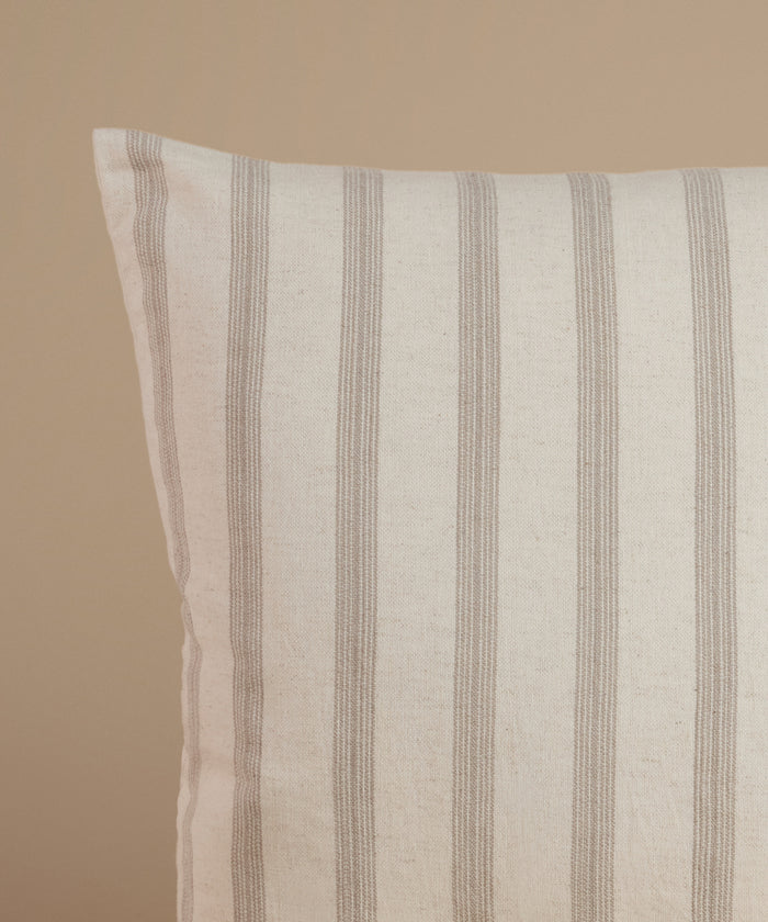 A white and tan stripe pillow against a beige background.