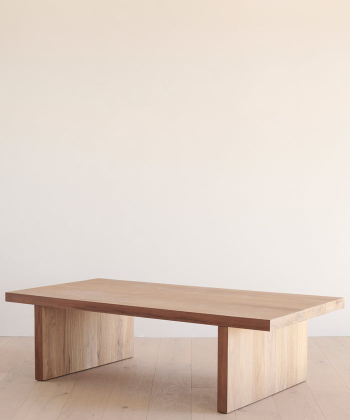 A minimalist wooden coffee table with a rectangular top and sturdy legs, set against a simple backdrop, is easily protected when needed by the Outdoor Vista Coffee Table Cover.