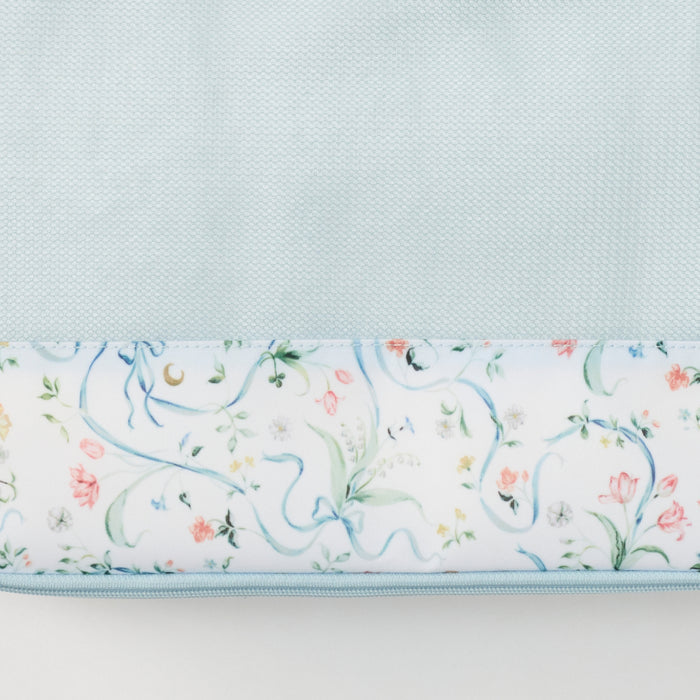 A close-up of a fabric item showing two sections: a solid pale blue textured upper section and a lower section with a white background and a delicate pastel floral and vine pattern in blue, pink, and green. A light blue zipper runs along the bottom edge.