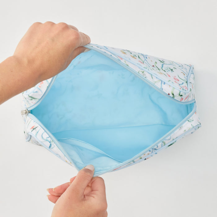 A light blue and white floral zippered pouch being opened by two hands, showing a bright light blue interior, on a plain white background.