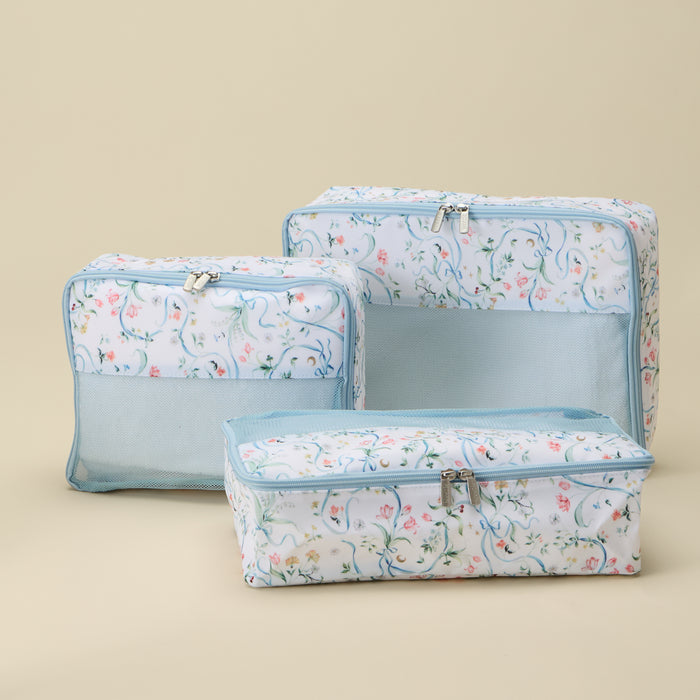 Three rectangular zippered travel or storage bags in a light blue and white floral print, arranged by size on a solid beige background.