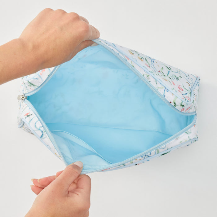 A light blue and white floral patterned zippered pouch shown open, with a person's hands holding the top and bottom edges to display the interior. The pouch has a solid light blue lining.