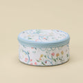 A round zippered cosmetic bag with a white background and a delicate multicolor floral pattern, featuring a light blue zipper and trim, set against a solid beige background.