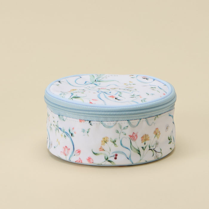 A round zippered cosmetic bag with a white background and a delicate multicolor floral pattern, featuring a light blue zipper and trim, set against a solid beige background.
